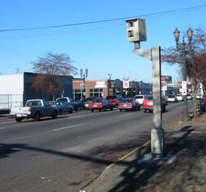 The photo shows a post-mounted enforcement camera that captures red light runners.