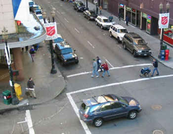 The picture shows a city street with a crosswalk and pedestrians with different speed characteristics. a person pushing a baby stroller and three pedestrians are crossing in this photo. 