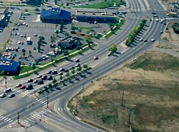 The picture shows a raised median on a six-lane divided arterial. A driveway into a large shopping center is located approximately 80 to 100 meters (240 to 300 feet) from signalized intersections on each side. The driveway access is restricted by the median to right-in/right-out/left-in. 