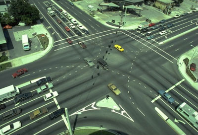 The picture shows a wide four-way signalized intersection with double left-turn lanes on all approaches. Dotted pavement lines are used to guide left-turning vehicles into the appropriate lanes.