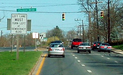 The picture shows a car in the left lane and a sign in the median that reads, “left lane must turn left at Democracy Boulevard.” 
