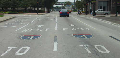 The picture shows an approach with pavement markings that read “to (symbolic I-4) East” in the rightmost through lane, “to (symbolic I-4) West” in the leftmost through lane, and “yield to peds” in the left-turn lane.