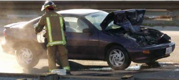 The picture shows a car that recently has been involved in a collision. Its hood is open, and a fireman is attending to the rear of the vehicle. 