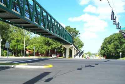 Figure 70. a pedestrian grade separation treatment. Photo. The picture shows a wide road with a median. A raised footbridge set on concrete piers provides a grade-separated crossing for pedestrians to eliminate conflicts with vehicles.