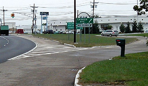 Figure 82. Example of jughandle and associated signing. Photo. The picture shows a jughandle exiting to the right in advance of a signalized intersection. White-hatched pavement markings are used in the gore area of the jughandle ramp to delineate through movements from right-turn movements. A white-on-green sign in the gore area of the ramp indicates -Carmen ave- in uppercase letters with an arrow pointing to the upper right. Below it, a black-on-white sign indicates "all turns" in uppercase letters with an arrow pointing to the upper right.