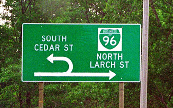 Figure 87. Example of median U-turn signing in Michigan. Photo. The picture shows a direction sign in advance of a U-turn location. The through arrow points north to Business 96 (Larch Street). The U-turn arrow points south to Cedar Street.