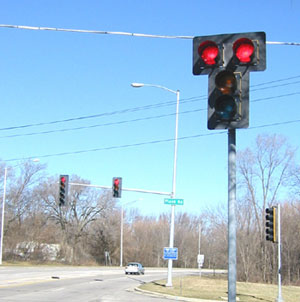 Figure 113. Signal head with a double red signal indication. Photo. The photo shows a signalized intersection with a signal head that has a double red signal indication on the near side of the intersection. The double red indications are positioned side-by-side and are centered above the vertical yellow and green indications.