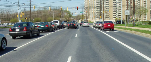 Figure 123. Narrow (2.4-meter (8-foot)) right-turn lanes may be used effectively in retrofit situations. Photo. This photo of a signalized intersection in an urban setting shows a narrow right-turn lane with a sign that reads "right lane must turn right" in uppercase letters. Four cars wait in the queue to turn right.