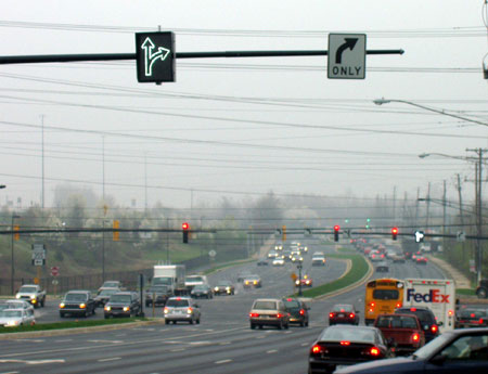 Figure 126. Example of variable lane use sign to add a second right-turn lane along a corridor during certain times of day. Photo. The picture shows fiber optic variable lane use signs on a mast arm in advance of the intersection and on the signal mast arm at the intersection. The variable sign shows a shared through-right movement and is located to the left of a fixed sign indicating right turn only.