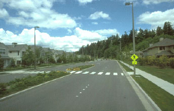 Figure 31 Photo. Raised medians and crossing islands can improve pedestrian safety on multilane roads. This photo shows a road with two lanes in each direction with a raised median in the center of the road and a wide crosswalk cutting through it.