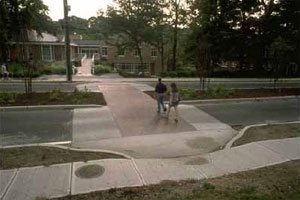 Figure 36. Photo. Raised crosswalks can control vehicle speeds on local streets at pedestrian crossings. This photo shows a two-lane roadway with a raised median and a raised crosswalk at midblock. Two pedestrians are crossing in the crosswalk.