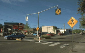 Figure 39. Photo. Pedestrian warning signs sometimes are used to supplement crosswalks. This photo is the same photo as shown in figure 5. It shows a lone pedestrian in a crosswalk that is marked by three different yellow and black signs with the crosswalk symbol-one on each side of the street, and one directly over the middle of the crosswalk.