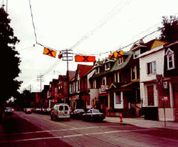 Figure 9.  Photo. Example of overhead crosswalk sign used in Canada.  This photo shows a street with crosswalk marking signs that are hanging overhead. There are three signs, two of which are yellow; the middle sign is orange. All three have a large X on them.