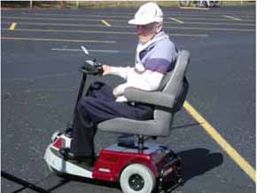 Figure 10: Photo. Assistive powered scooter. A man is in an assistive powered scooter in a parking lot.