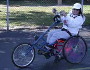 Figure 12: Photo. Another hand cycle. A woman is using a hand cycle to travel in a parking lot.