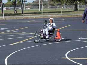 Figure 28: Photo. Participant within turning radii station. A participant is riding a hand cycle through a curved turning path delineated in a parking lot.