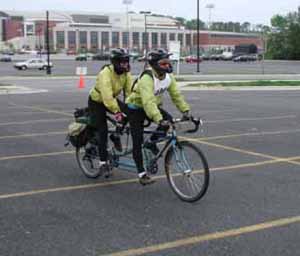 Figure 4: Photo. Tandem bicycle. Two adults are riding a tandem bicycle in a parking lot.