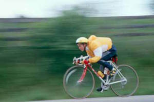 Figure 47: Photo. AASHTO's design bicyclist travels at 30 kilometers/hour (20 miles/hour). A bicyclist is riding at a high rate of speed as indicated by the blurred green background behind him and his wind-filled jacket.