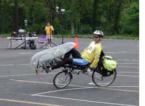 Figure 5: Photo. Recumbent bicycle. A man is riding a recumbent bicycle in a parking lot.