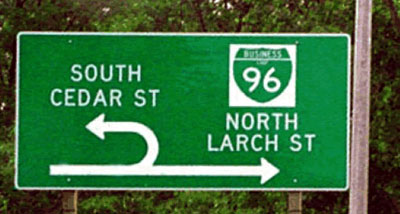 Figure 13a. Photo. Example 1 of innovative signing. Photo shows a directional sign in advance of a U-turn location. The through arrow points north to Business 96 (Larch Street). The U-turn arrow points south to Cedar Street.