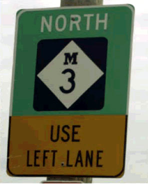 Figure 13d. Photo. Example 4 of innovative signing. Photo of graphical sign in advance of a U-turn location that indicates North Michigan Highway 3-USE LEFT LANE.