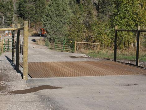 This picture shows deer-proof fencing, paralleling a highway, that abuts an approach road. The surface of the approach road between these fence ends is a colored metal grate used to prevent animals from getting on the other side of the fence through this approach road.