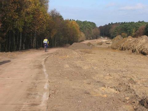 This is a picture of road deconstruction. Where a road once went, there is rough graded earth and a winding bicycle path. A bicyclist rides down the path.