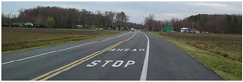 Figure 1. Photo. Example of a Rural STOP AHEAD Installation. This photo shows the words stop ahead painted on the road surface. The words are in order as you approach, so that ahead is above stop.