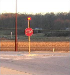 Figure 2. Photo. Example of a STOP Sign Mounted Flashing Beacon. Picture of a STOP sign with a flashing light mounted atop it on an extension of the post.