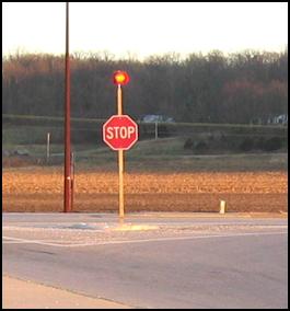 Figure 2. Photo. Example of a STOP Sign Mounted Flashing Beacon. A STOP sign is shown with a flashing light on the same pole, placed above the sign, at a rural intersection.