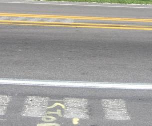 This figure shows an implementation of concept 1 at site 1 in Florida. The photo shows a section of the major road looking across the road from shoulder to shoulder. Shoulder rumble strips are shown, starting approximately 1.5 m (6 inches) from the edge line and continuing toward the edge of the shoulder. A painted median is installed along with median rumble strips that fully cover the width of the median between the inside edges of the pavement markings. A double solid yellow pavement marking is installed along each side of the median rumble strips, and raised pavement markings are installed along these centerlines. 