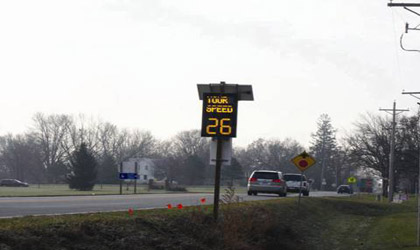 Photograph showing a dynamic speed feedback sign in Slater, Iowa. The sign diplays YOUR SPEED 26 in yellow lights against a black background. The number 26 is much larger than the word legend. A stop ahead sign and school crossing symbol sign can be seen in the background.