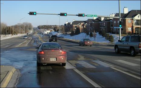 Figure 3. Photo. Example of a type 2 installation in Lincoln NE (lateral separation with no offset). The photo shows an approach to a signalized intersection with lateral separation with no offset. The lateral separation is created with pavement markings, which separate the left-turn lane approximately 1.8 m from the two adjacent through lanes. There is a raised concrete median separating the left-turn lane from the two opposing through lanes. There is a car in the near-side left-turn lane, and it appears that the driver of the left-turning vehicle has improved sight distance into the opposing through lanes compared to a driver of a vehicle at an intersection with no offset and no lateral separation. However, there is no car in the opposing left-turn lane, so it is difficult to observe the apparent sight distance improvement.