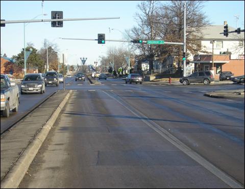 Figure 4. Photo. Example of a type 3 installation in Lincoln, NE (lateral separation with negative offset). The photo shows an approach to a signalized intersection with lateral separation with a negative offset. The lateral separation is created with pavement markings, which separate the left-turn lane approximately 0.6 m from the two adjacent through lanes. There is a raised concrete median separating the left-turn lane from the two opposing through lanes. There is no car in the near-side left-turn lane, but there is a car in the far-side left-turn lane, and it appears that the driver of a left-turning vehicle has less sight distance into the opposing through lanes compared to a driver of a vehicle in an intersection with no offset.