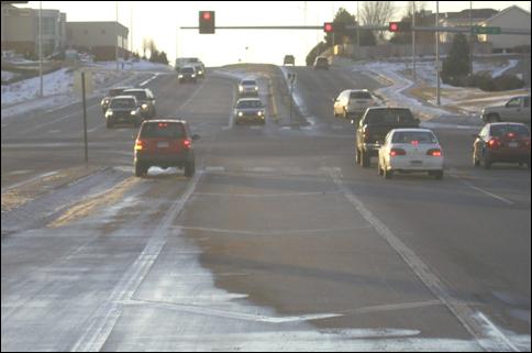 Figure 2. Photo. Example of a type 1 installation in Lincoln, NE (positive offset). The photo shows an approach to a signalized intersection with positive offset left-turn lanes. The positive offsets are created with pavement markings, which separate the left-turn lanes approximately 3.6 m from the two adjacent through lanes. There is a raised concrete median separating the left-turn lane from the two opposing through lanes. There are cars in both left-turn lanes traveling in opposite directions, and it is clear that the drivers of the opposing left-turn vehicles can see clearly into the opposing through lanes.
