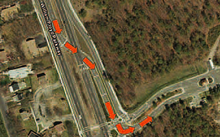 Figure 2. Photo. Left-turn crossover movement at a 3-legged partial DLT intersection in Shirley, NY. The figure shows a left-turn crossover movement at a 3-legged partial displaced left-turn (DLT) intersection in Shirley, NY. There are orange arrows in the photograph which represent the left-turn crossover movement.
