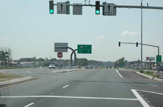 The photo shows a continuous flow intersection overhead sign at a displaced left-turn (DLT) intersection in Baton Rouge, LA.