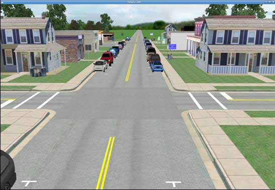Parked cars condition. The figure depicts a simulator screenshot of the parked cars town condition. It shows a daytime view of a two-lane undivided main roadway running down the center of a small town. The town consists of small homes and stores lining the main roadway. A standard intersection is clearly visible in the foreground, and a second intersection is barely visible in the background. All roadways in the town have curbs, gutters, and sidewalks. They also have double yellow centerlines which are interrupted at the intersections. The minor intersecting roadway running horizontally across the screen has marked crosswalks and stop bars on either side. Marked parking spaces are visible on either side of the main roadway, but, unlike the baseline condition, cars are parked in most of the parking spaces on both sides of the street along the main roadway through the town.