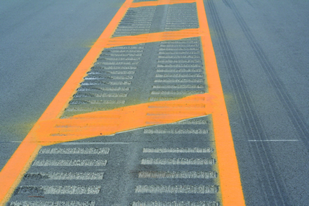 Figure 5. Photo. Two rows of rumble strips in the median. The figure shows a photo of a two-way road, with one travel lane in each direction. The photo is taken down the center of a road, which has a yellow median with yellow ladder marks. There are also two rows of rumble strips running parallel to each other within the median on the left and right sides. The yellow median narrows off into a centerline in the distance.