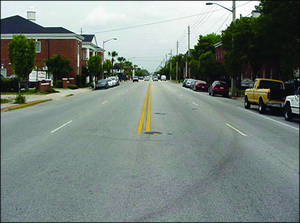 Figure 1. Photo. Four-lane configuration before road diet. (Source: Pedestrian Bike Information Center, Road Diets training module, 2009). This picture shows a four-lane, undivided roadway in an urbanized area with two through lanes in each direction and cars parked on each side of the road.