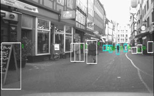 This photo shows true detections and typical false positives. People are tracked using white and teal bounding boxes. The white boxes indicate possible pedestrian objects, and the blue boxes indicate possible pedestrian objects to be further analyzed by an appearance classifier.