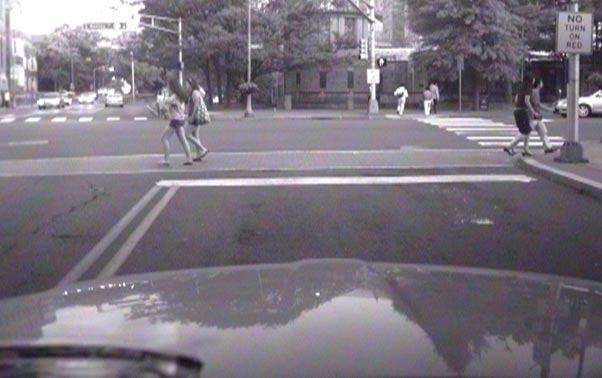 This photo shows pedestrians crossing a signalized intersection in an urban environment during the day. There are many vehicles on the road, and the road has sidewalks.