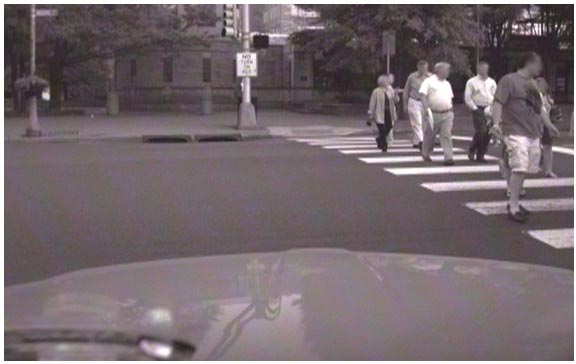 This photo shows pedestrians crossing the street at a signalized intersection in an urban environment. There is a vehicle waiting for the pedestrians to cross before turning right.