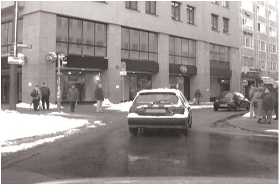 This photo shows people walking on the sidewalk on both sides of a street in an urban environment as a vehicle drives down the street.