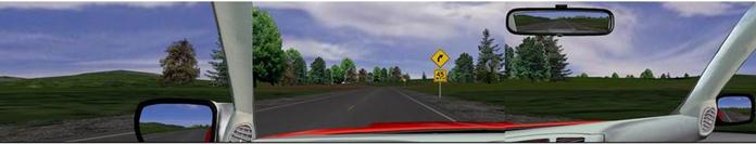 Figure 6. Screenshot. Example curve before the curve warning sign and advisory speed panel. This image is a composite developed from the three screens of the simulator. The view appears to be out the front and side windows of a vehicle driving on a rural road. A curve can be seen on the horizon, and there is a curve warning sign and 45-mi/h advisory speed panel on the right side of the road ahead.
