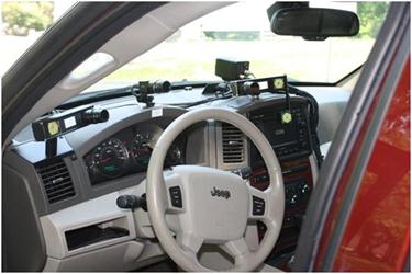 The dashboard of a sport utility vehicle is shown. There are three cameras with their lenses oriented toward the location where the driver's face would be. The center camera is above the instrument panel and directly in front of the driver. The other two cameras are about 1.5 ft (0.46 m) from either side of the center camera. The outboard cameras have a small hexagonal array of infrared light-emitting diodes attached to their mounts.