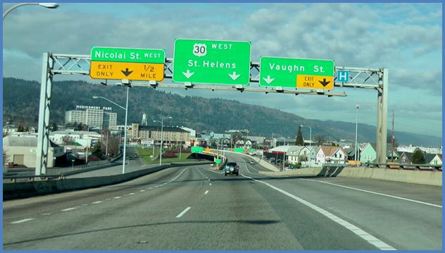 This photo shows a driving image for scenario 1 critical point 3. There is a four-lane single direction highway. There are four signs shown. On the left-most sign, the top half is green and labeled  Nicolai St. West,  and the bottom half is yellow with a down arrow and is labeled  Exit Only 1/2 mile.  The second sign is green and has two down arrows. The top of the sign has a label for  30 West.  Below it and above the arrows there is a label for  St. Helens.  The third sign is green with two down arrows. The right down arrow is surrounded by a yellow box that is labeled as an exit only lane. Above both arrows, there is a label for Vaughn St. The fourth sign is a small blue sign with the letter  H  to indicate hospital.