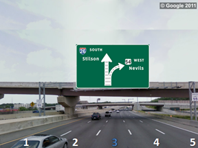 This photo shows a split with an odd number of lanes on a five-lane highway. The lanes are numbered 1 through 5 from left to right, with 3 highlighted in blue. There is a sign above the roadway showing a five-lane up arrow labeled  26 South Stilson.  Two lanes (4 and 5) curve to the right and are labeled  54 West Nevils.  The remaining three lanes (1 through 3) continue straight.