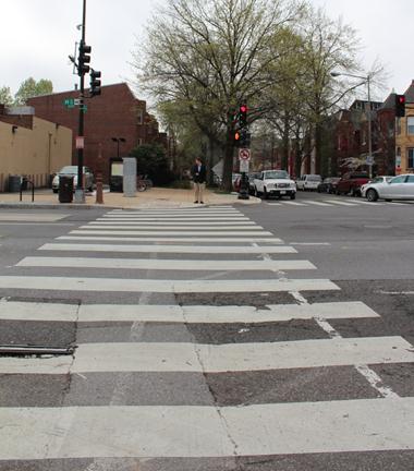 Illustration of what a pedestrian might see as he or she attempts to cross from the north side of H Street Northeast to the south side of the street along 3rd Street Northeast. A pedestrian waiting to cross to the north side of the street can also be seen looking for oncoming traffic.