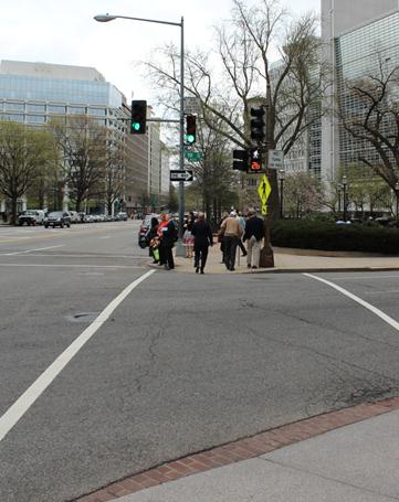 Illustration of what a pedestrian might see as he or she attempts to cross from the west side of 19th Street Northwest to the east side of the street along Pennsylvania Avenue Northwest. The photograph is taken from the perspective of the pedestrian. A few pedestrians are completing their crossing.